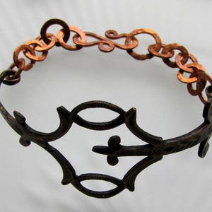 May include: A copper bracelet with a decorative, intricate design. The bracelet is made of linked circles and a detailed, openwork design in the center.