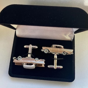May include: A pair of cufflinks in a black velvet box. The cufflinks are silver and feature a miniature car design. One cufflink shows the car from the side, while the other shows the car from the back.