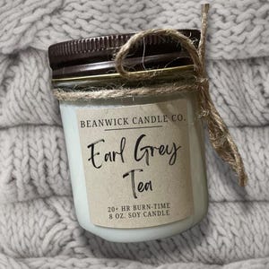 Peut inclure: Une bougie en pot de verre avec un couvercle marron et une étiquette indiquant "Earl Grey Tea". La bougie est attachée avec de la ficelle. L'étiquette indique également "20+ HR BURN-TIME 8 OZ. SOY CANDLE". La bougie est de Beanwick Candle Co.