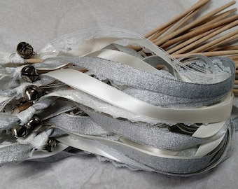 May include: A bundle of white and silver ribbon wands with bells attached to the ends. The wands are made of wooden dowels and are tied together with white ribbon.