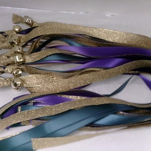 May include: A bundle of wedding ribbon wands with teal, purple, and gold glitter ribbon. Each wand has a small bell attached to the end.