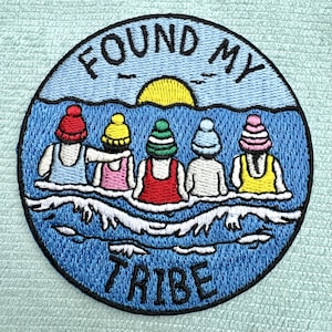 Könnte beinhalten: Ein runder gestickter Aufnäher mit fünf Figuren in Badeanzügen und Strickmützen im blauen Wasser. Darüber ein gelber Sonnenkreis und der Text FOUND MY, darunter der Text TRIBE. Die Figuren tragen rote, gelbe, grüne, weiße und rosafarbene Mützen.