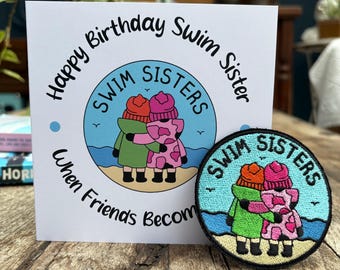 May include: A greeting card and patch with the text "Happy Birthday Swim Sister" and "Swim Sisters." The card and patch feature an illustration of two figures hugging, wearing coats and hats. The patch is round with a blue border.