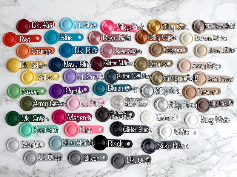 May include: A collection of 36 small, round, colorful buttons with various names written on them. The buttons are arranged in rows and columns on a white surface.