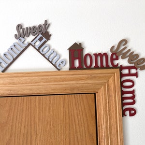 comparing the new larger home sweet home door decoration with the regular sized one on a door frame