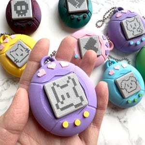 May include: A collection of colorful, handheld digital pet toys in various colors, including purple, yellow, and green. Each toy features a pixelated pet design on a gray screen and a small metal chain for attachment.