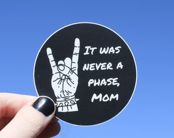 May include: Black and white sticker with a hand making the rock and roll sign. The sticker says "It was never a phase, Mom".