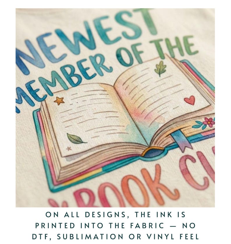 Puede incluir: Primer plano de una tela color crema con una colorida ilustraci&oacute;n de un libro abierto con el texto "NEWEST MEMBER OF THE BOOK CLUB". El libro tiene un dise&ntilde;o de estrella, hoja y coraz&oacute;n. El texto en la parte inferior dice: "ON ALL DESIGNS, THE INK IS PRINTED INTO THE FABRIC - NO DTF, SUBLIMATION OR VINYL FEEL."