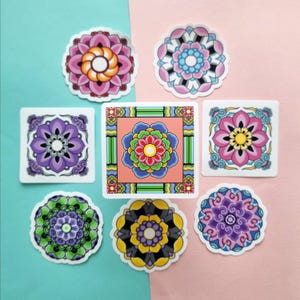 Puede incluir: Una colección de pegatinas florales coloridas con diseños intrincados. Las pegatinas presentan varias formas, incluyendo círculos y cuadrados, y una gama de colores como rosa, morado, verde, amarillo y azul. El fondo está dividido entre una superficie azul claro y rosa.