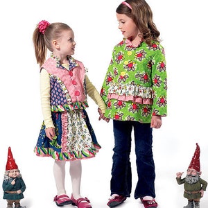 May include: Two young girls wearing colorful patterned dresses and jackets. One girl is wearing a green jacket with a floral pattern and the other is wearing a pink and blue patchwork vest. Both girls are standing next to two small gnome figurines.