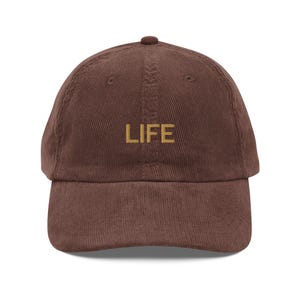 May include: A brown corduroy baseball cap with the word "LIFE" embroidered in gold on the front.