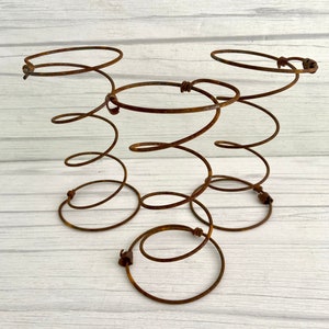 May include: Three rusty metal bed springs, each with a circular top, are arranged in a triangular formation on a white wooden surface.