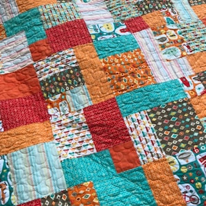 May include: A patchwork quilt with a variety of colorful squares in shades of orange, red, teal, and brown. The squares feature different patterns, including polka dots, stripes, and geometric designs.