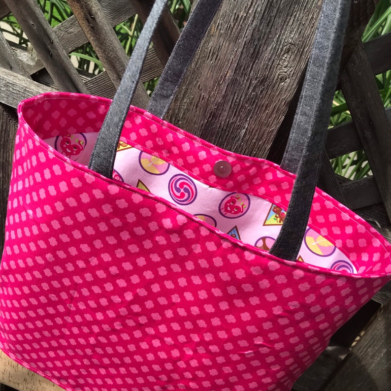 May include: A pink tote bag with a polka dot pattern. The bag has black straps and a pink and white patterned lining.