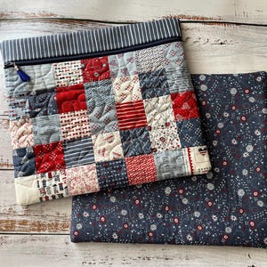 Puede incluir: Un estuche acolchado con cremallera que presenta un dise&ntilde;o de patchwork de cuadrados de tela rojos, blancos y azules con varios patrones, rematado con un borde a rayas azul marino y blanco y una borla azul, junto a una pieza de tela azul oscuro.
