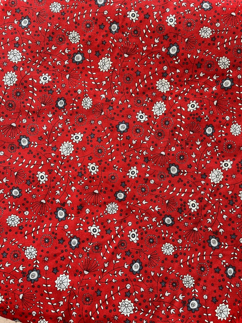 May include: Red fabric with a repeating floral pattern. The design features white and gray flowers, small stars, and delicate stems with tiny leaves. The background is a solid, vibrant red.