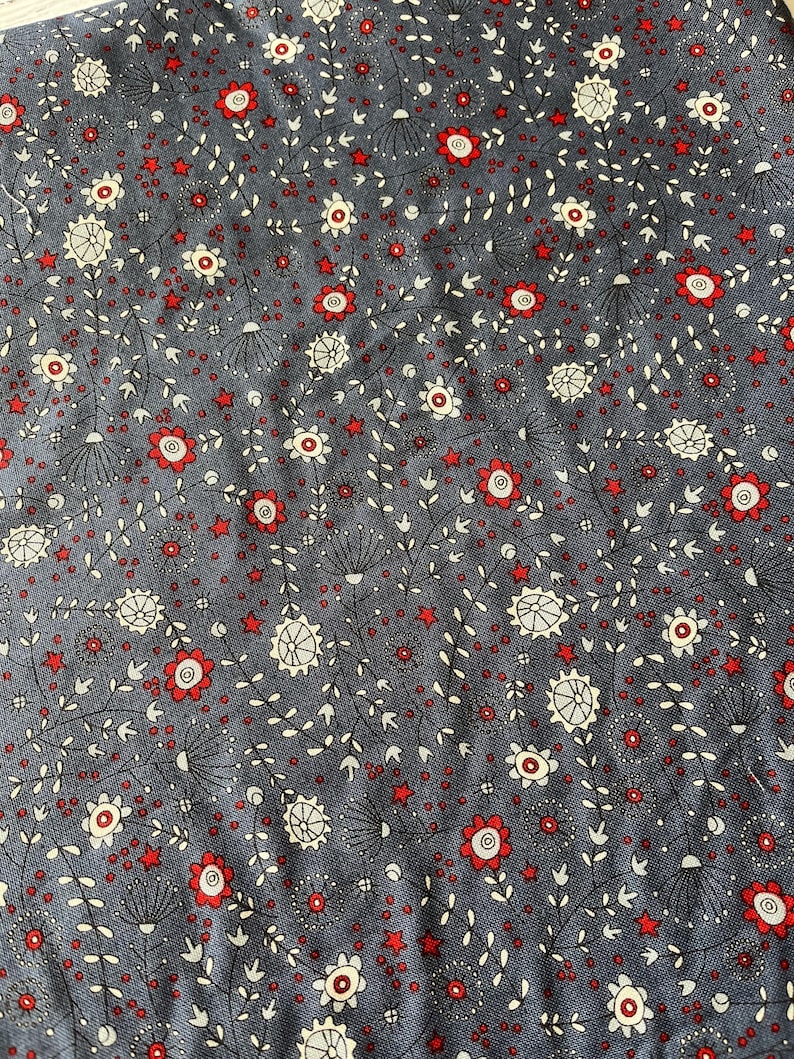 Puede incluir: Una tela gris oscuro con un patr&oacute;n repetitivo de peque&ntilde;as flores rojas, motivos florales circulares blancos y diminutas estrellas rojas. El dise&ntilde;o incluye tallos y hojas negras finas que conectan los elementos florales.