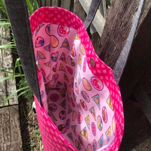 May include: Pink tote bag with a black strap and a pink and white patterned lining featuring cartoon characters and geometric shapes.