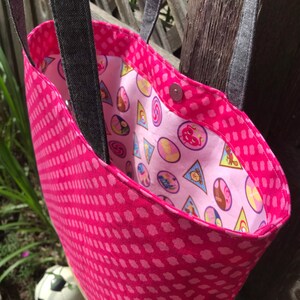 May include: Pink tote bag with a pink and white polka dot pattern on the outside and a pink and white patterned lining on the inside. The bag has two black straps.