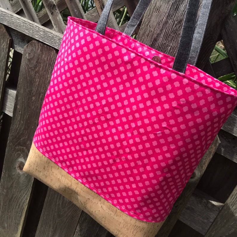 May include: A pink tote bag with a white polka dot pattern and a cork bottom. The bag has black straps.