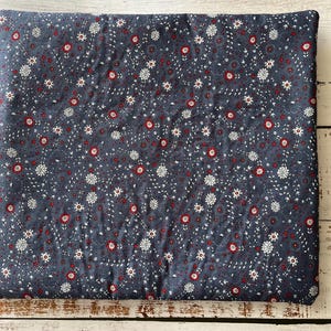 Puede incluir: Un coj&iacute;n de tela cuadrado con un fondo gris oscuro y un patr&oacute;n repetitivo de peque&ntilde;as flores blancas y diminutos acentos circulares rojos. El tejido tiene una textura acolchada con l&iacute;neas de costura visibles en toda la superficie.