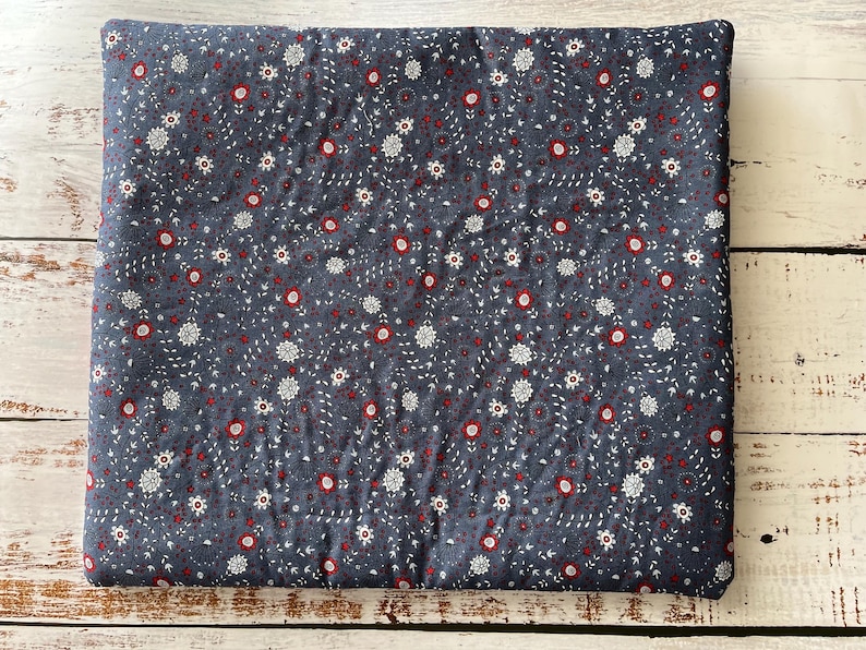 Puede incluir: Un coj&iacute;n de tela cuadrado con un fondo gris oscuro y un patr&oacute;n repetitivo de peque&ntilde;as flores blancas y diminutos acentos circulares rojos. El tejido tiene una textura acolchada con l&iacute;neas de costura visibles en toda la superficie.