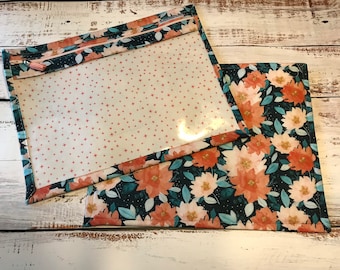 May include: Two fabric pouches with a zipper closure. The pouch on the left has a clear plastic window and a white background with small pink stars. The pouch on the right has a dark blue background with a floral pattern in shades of pink, orange, and green.