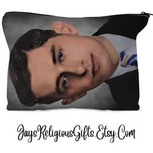 May include: A black zippered pouch featuring a portrait of a man in a suit and tie. The man has dark hair and is looking towards the viewer. The pouch has a black zipper and a gray background.
