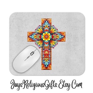 May include: A decorative mousepad featuring a colorful cross design with floral accents in shades of red, yellow, blue, and orange. A white computer mouse is positioned to the left of the cross. The mousepad has a light gray background.