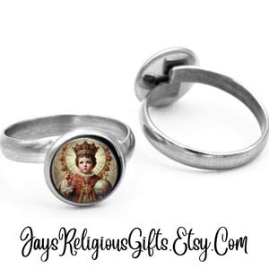 May include: Two silver-toned rings. One ring features a round image of a crowned figure holding a globe and a cross. The other ring is shown separately. The text "JaysReligiousGifts.Etsy.Com" is at the bottom.