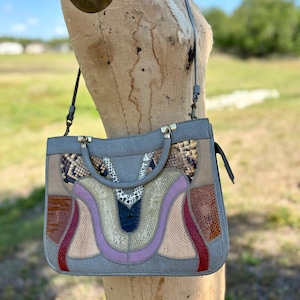 May include: Gray handbag with a patchwork design featuring various textures and colors, including snake print, tan, red, and purple. The bag has a top handle and a shoulder strap, with gold-colored hardware.