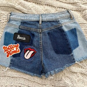 May include: Denim shorts with a patchwork design in various shades of blue. Patches include the text "Ronnie" and the Rolling Stones logo. The shorts have a frayed hem.