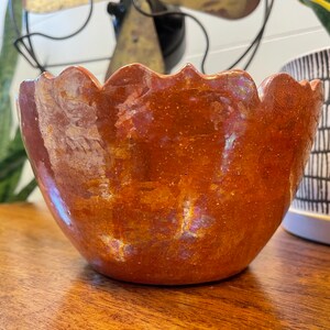 May include: A small, scalloped, terracotta-colored ceramic bowl with a iridescent glaze. The bowl has a rustic, handmade look.