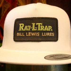 May include: White trucker hat with a black patch that says "Rat-L-Trap. Bill Lewis Lures" in yellow and brown lettering.