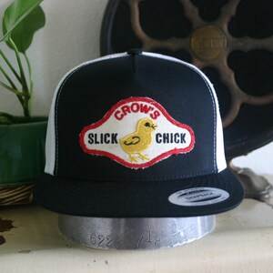 May include: Black and white trucker hat with a red, white, and yellow embroidered patch that says "CROW'S SLICK CHICK".