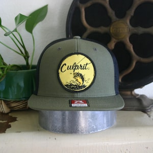 May include: A green and black trucker hat with a yellow patch that says "Culprit" and features a cartoon fish. The hat has a black mesh back.