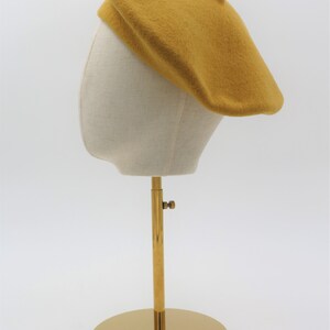 May include: A mustard yellow beret on a white mannequin head with a gold metal stand.