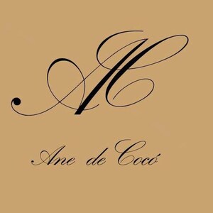 May include: A logo design featuring the stylized initials "AC" in elegant black script atop the words "Ane de Coco" in a matching font. The background is a solid tan color.