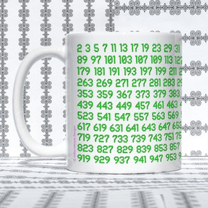 May include: White ceramic mug with a green design of numbers from 2 to 953. The numbers are arranged in rows and columns.