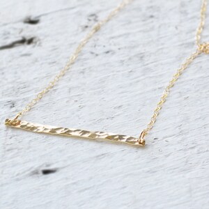 A delicate gold filled necklace with a hammered bar pendant. The chain is thin and delicate, and the bar is simple and elegant.