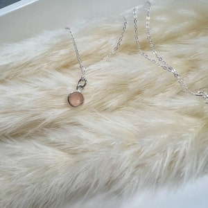 Puede incluir: Un delicado collar de cadena de plata con un peque&ntilde;o colgante redondo de piedra preciosa rosa claro.