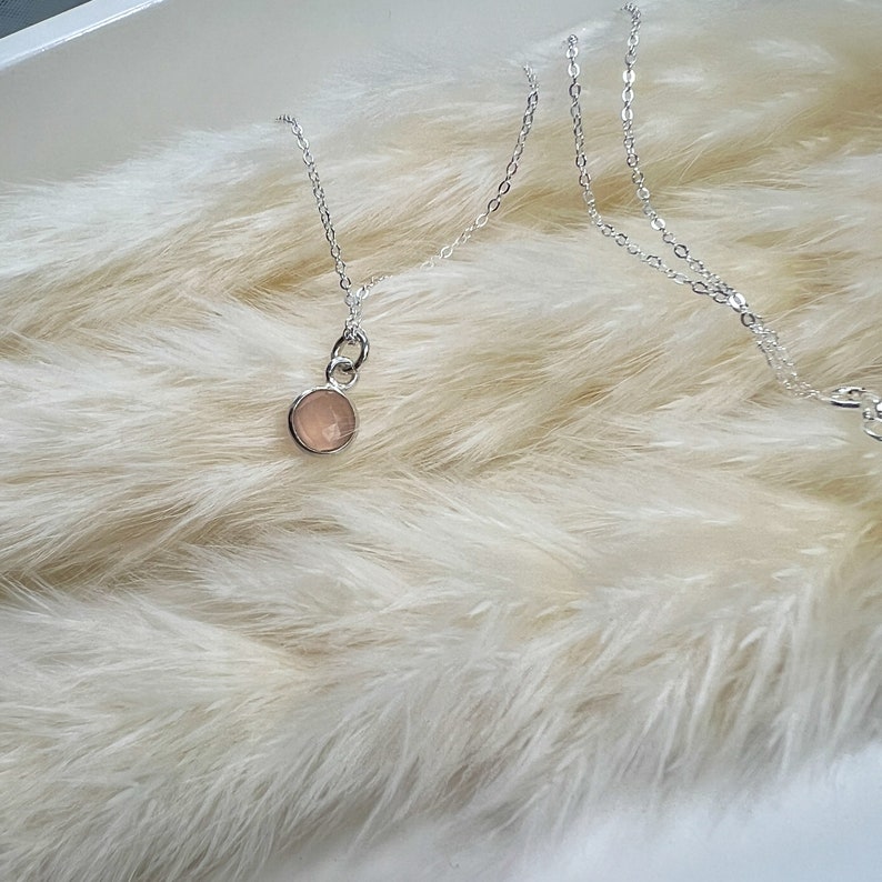 Puede incluir: Un delicado collar de cadena de plata con un peque&ntilde;o colgante redondo de piedra preciosa rosa claro.