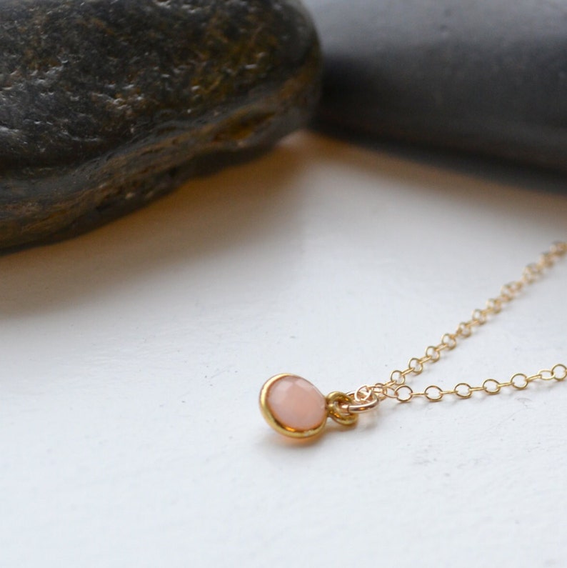Puede incluir: Un delicado collar de cadena de oro con un peque&ntilde;o colgante redondo de piedra preciosa rosa p&aacute;lido.