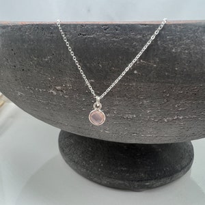 Puede incluir: Un delicado collar de cadena de plata con un peque&ntilde;o colgante redondo de piedra preciosa rosa claro.