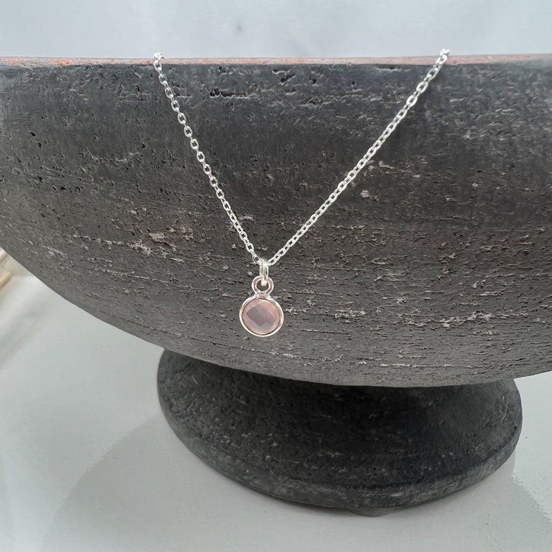 Puede incluir: Un delicado collar de cadena de plata con un peque&ntilde;o colgante redondo de piedra preciosa rosa claro.