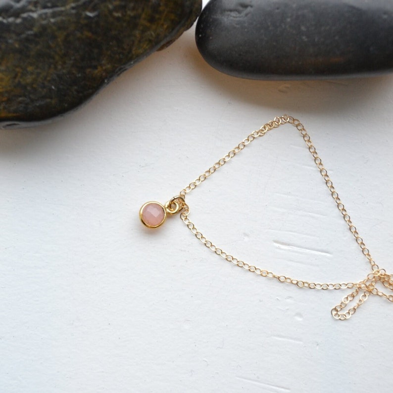 Puede incluir: Un delicado collar de cadena dorada con un peque&ntilde;o colgante redondo de piedra preciosa rosa claro.