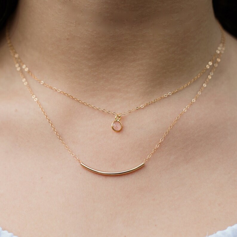 Puede incluir: Un delicado collar de oro con un peque&ntilde;o colgante de piedra preciosa rosa y un colgante de barra de oro fina.