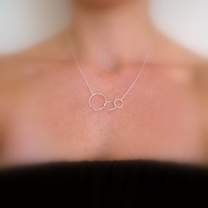 May include: A silver necklace with three interlocking circles, the largest circle is in the center and the two smaller circles are on either side.
