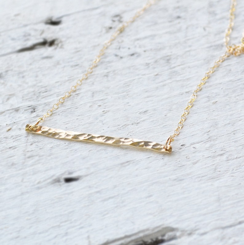 A delicate gold filled necklace with a hammered bar pendant. The chain is thin and delicate, and the bar is simple and elegant.