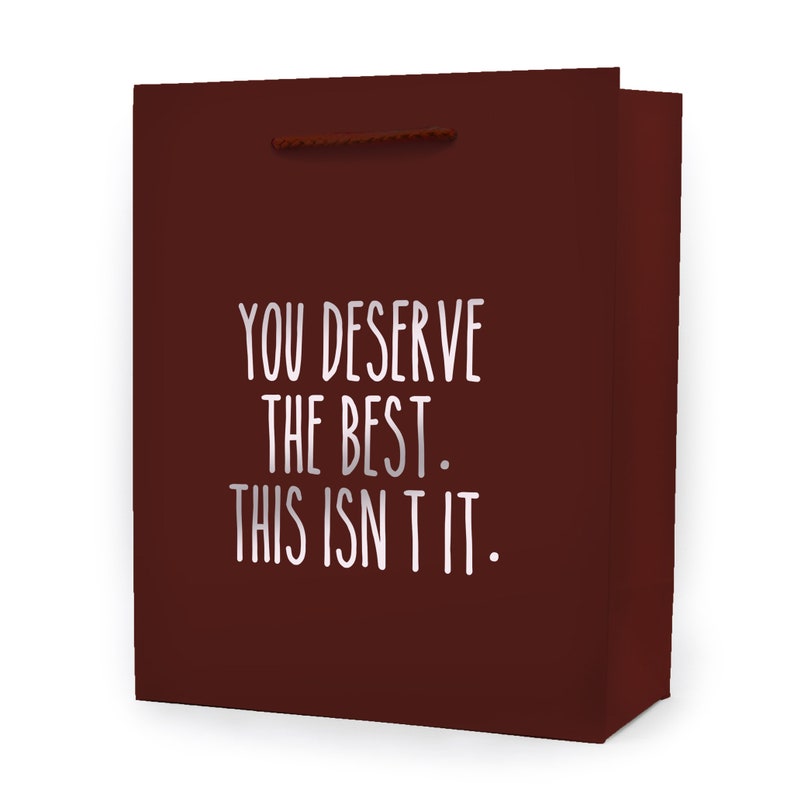 May include: A maroon gift bag with a white and gray text that reads "YOU DESERVE THE BEST. THIS ISN'T IT." The bag has a brown rope handle.
